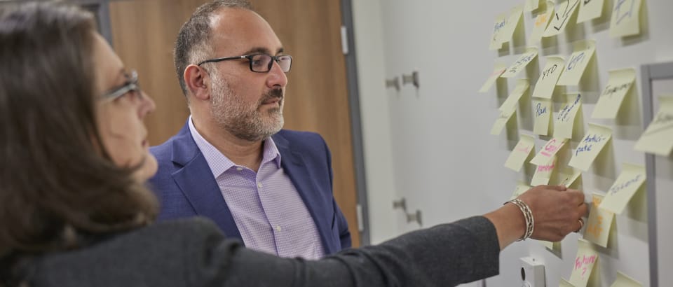 Two people look at a whiteboard filled with sticky notes